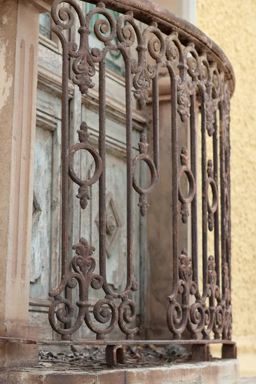 Barandal de hierro forjado con volutas frente a un muro ocre